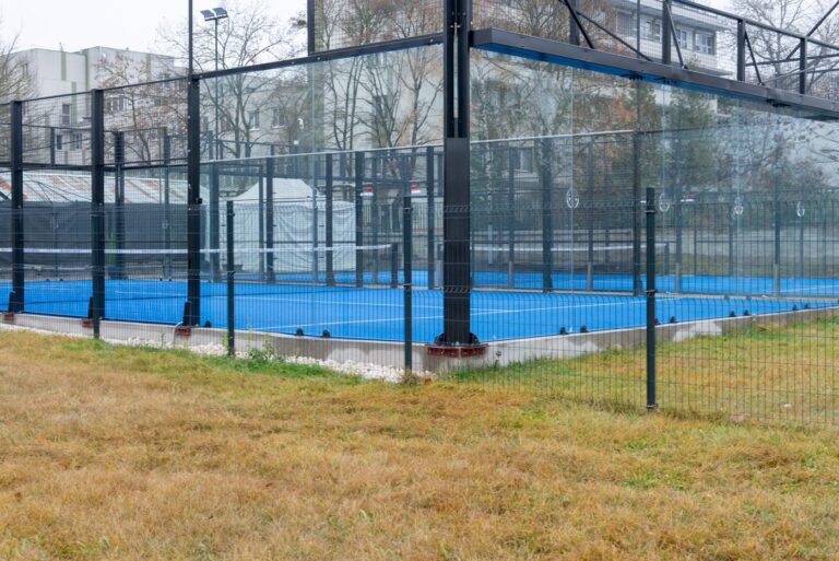 Terrain de padel outdoor avec surface bleue, structure métallique, grillage et panneaux vitrés